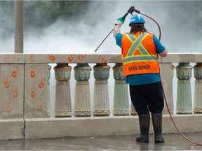 A worker uses a pressure washer to remove orange handprints from the Albert Street bridge in Regina on July 5, 2021. The handprints were painted on the bridge following the discoveries of unmarked graves in Kamloops and on Cowessess First Nation.