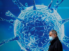 A man wearing a protective face mask walks past an illustration of a virus outside a regional science centre amid the coronavirus disease (COVID-19) outbreak, in Oldham, Britain.