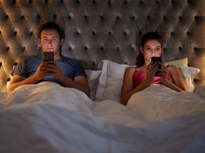 Couple Lying In Bed Checking Mobile Phones Whilst Ignoring Each Other