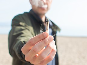 Young man holding a lit marijuana joint while smoking on the beach. Blur background and copy space right.