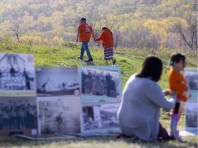 A couple holds hands during an event on the National Day for Truth and Reconciliation on Thursday, September 30, 2021 on the Cowessess First Nation. In the foreground are images of children at residential school.