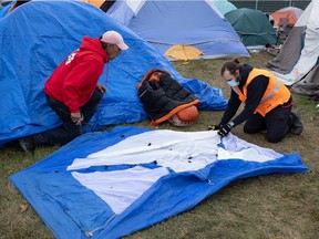 Volunteers Randy Netmaker, left, and Ian Betz-Wood set up another tent at Camp Marjorie, a tent encampment housing homeless people, in Pepsi Park in Regina, Saskatchewan on Oct. 25, 2021. Betz-Wood said it was the fourth tent set up during the day. Winds and general wear and tear have caused damage to some tents within the camp.