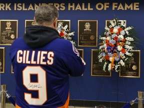 A fan stops to view the flowers surrounding the Hall of Fame plaque of former New York Islanders captain Clark Gillies prior to the game against the Toronto Maple Leafs at UBS Arena on Saturday in Elmont, New York. Gillies, who died on Friday, served as the Islanders' captain from 1977 to 1979. He helped the Islanders win the Stanley Cup in 1980, 1981, 1982 and 1983.
