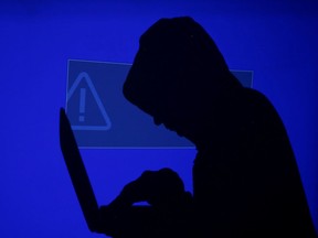 A hooded man holds a laptop computer as blue screen with an exclamation mark is projected on him in this illustration picture taken on May 13, 2017. REUTERS/Kacper Pempel/Illustration/file Photo