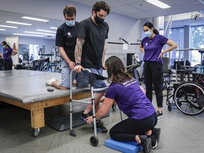 Humboldt Broncos bus crash survivor Ryan Straschnitzki, centre, is helped to stand in a walker by Eric Daigle, left, and Jill Mack, centre right, while he attends a physiotherapy session in Calgary, June 24, 2021.