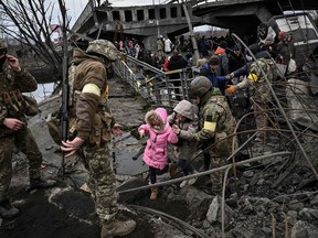 People cross a destroyed bridge as they evacuate the city of Irpin, northwest of Kyiv, during heavy shelling and bombing on March 5, 2022, 10 days after Russia launched a military invasion on Ukraine.