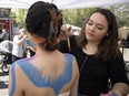 Artist Jayda Delorme paints model Kiana Francis's body during the Cathedral Village Arts Festival street fair on 13th Avenue.