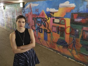 Erickka Patmore poses by a mural she painted at the pedestrian tunnel at the Albert St. bridge. Patmore's mural, which shows a stylized Cathedral Village street scene, was completed in 2021. Her mural, among others, was recently vandalized.