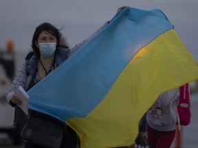 Un réfugié ukrainien arrivé à Regina à partir d'un vol humanitaire en provenance de Varsovie, en Pologne, se tient debout sur le tarmac, tenant un drapeau ukrainien.