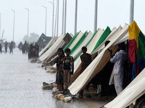 People who fled their flood hit homes stand outside temporary tents set along a road during a heavy monsoon rainfall in Sukkur of Sindh province, on August 27, 2022.