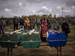 A priest blesses the remains of three people who died during the Russian occupation and were disinterred from temporary burial sites in Bucha, on the outskirts of Kyiv, on Wednesday, April 27, 2022.