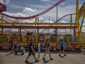 Attendees walk past a roller coster during the Queen City Ex at the REAL District on Wednesday, August 3, 2022 in Regina.