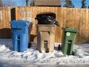 Tempat sampah hijau dari proyek percontohan kompos Kota Regina terlihat di sebelah tempat sampah daur ulang dan rumah tangga di sebuah gang di lingkungan Pusat Utara di Regina.