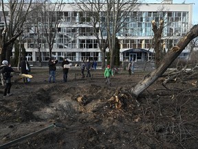 Bystanders look at a crater next to an educational building in Kyiv on Jan. 1, 2023, which was damaged by a missile strike on the previous day, amid the Russian invasion of Ukraine.