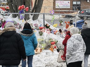 People stand next to a memorial at the site of a daycare centre in Laval, Que, Thursday, February 9, 2023, where a bus crashed into the building killing two children.