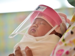 This file photo taken on April 9, 2020 through a glass window at a maternity ward shows a newborn baby wearing a face shield, in an effort to halt the spread of the COVID-19 coronavirus, at Praram 9 Hospital in Bangkok.