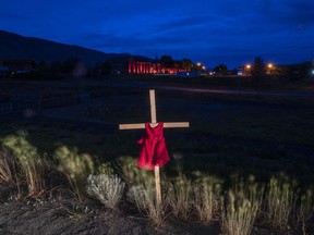 A child's dress is seen on a cross outside the Residential School in Kamloops, B.C., Saturday, June, 13, 2021. The shishalh Nation on British Columbia's Sunshine Coast says ground-penetrating radar has identified what are believed to be 40 unmarked graves of children on the site of the former St. Augustine's Residential School.