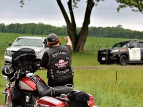 A man wearing an Outlaws motorcycle club vest gives the middle finger to an Ontario Provincial Police officer conducting an investigation at a house on Parkhouse Drive in Melbourne, southwest of London, on Tuesday, June 27, 2023. (Dale Carruthers/The London Free Press)