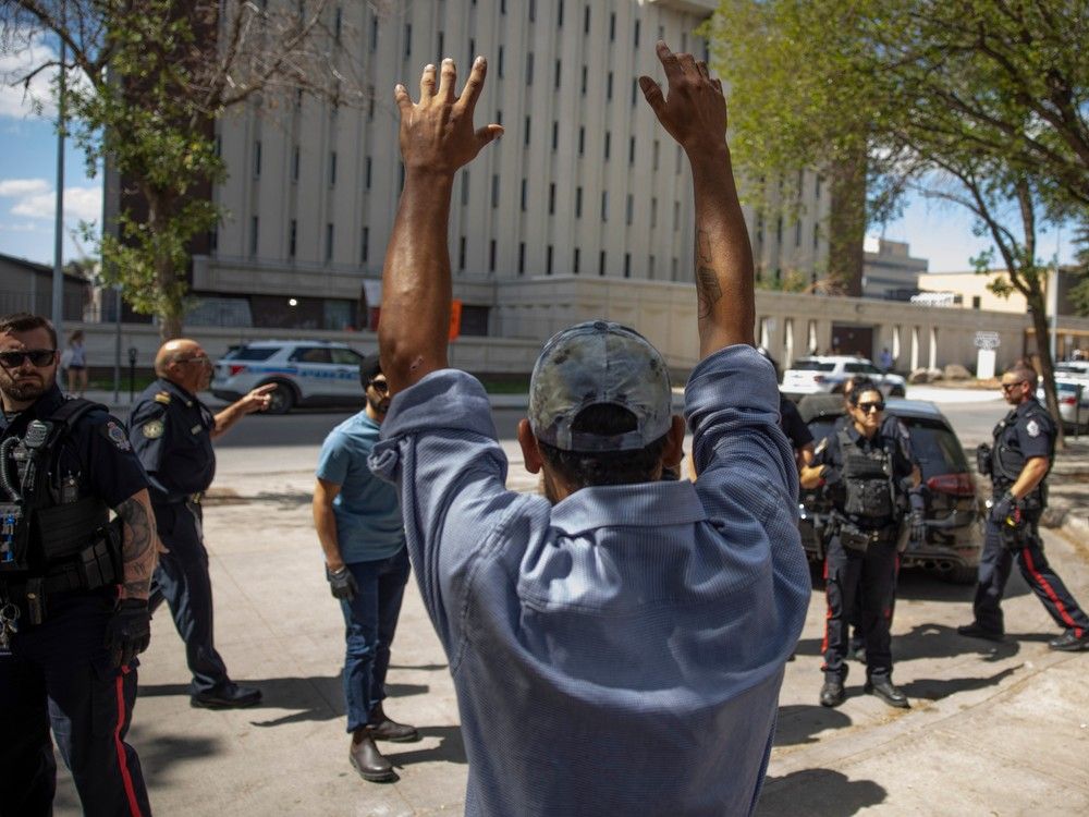 A man throws his hands in the air in front of the Regina Police Service, as camp members are told that they need to be vacated from City Hall in the next 24 hours on July 27, 2023, as a push to dismantle the pop-up encampment thats has held around eighty-five tents since it gathered in June. 