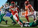 Saskatchewan Roughriders defensive back Jayden Dalke, left, looks on as Calgary Stampeders running back Ka'Deem Carey, centre, escapes the grasp of linebacker Micah Teitz during second half CFL football action in Calgary, Friday, Oct. 13, 2023.