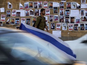 An Israeli soldier walks past images of Israeli hostages snatched by the Palestinian militant group Hamas last week in a surprise attack into Israel, plastered on a wall outside the Ministry of Defense in Tel Aviv on October 16, 2023.