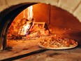 Pizza is cooked in a wood-fired oven.