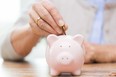 Stock photo illustration on savings, money, annuity insurance, retirement and people concept - close up of senior woman hand putting coin into piggy bank. Getty Images/iStock Photo