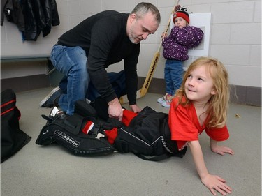 Mike Grimbleby, convenor of the Oakridge Aeros initiation level hockey, fastens the pads on his daughter Abigail, 6, at Oakridge arena under the watchful eye of sister Hailey, 3. Watching  MORRIS LAMONT/THE LONDON FREE PRESS /POSTMEDIA NETWORK
