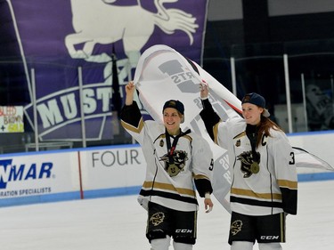 Manitoba Bisons Venia Hovi, left, and Caitlin Fyten skate the championship banner past the Mustang logo after winning the Women's Hockey National Championship 2-0 over Western at Western University's Thompson Arena on Sunday. MORRIS LAMONT/THE LONDON FREE PRESS /POSTMEDIA NETWORK
