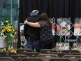 A man is comforted as he looks at photographs prior to a vigil on Sunday, April 8, at the Elgar Petersen Arena, home of the Humboldt (Sask.) Broncos, to honour the victims of a fatal bus accident.