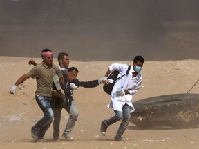 Palestinian protestors carry a wounded comrade during a protest near the border fence with Israel east of Jabalia in the central Gaza Strip on May 15, 2018. Palestinians were gathering today for fresh protests along the Gaza border, a day after Israeli forces killed dozens there as the US embassy opened in Jerusalem on what was the conflict's bloodiest day in years.