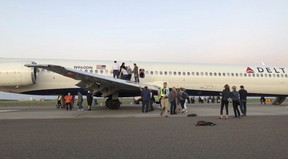 Passengers exit a plane and stand on the tarmac of Denver International Airport after being evacuated from a Delta flight from Detroit on Tuesda in Denver. A Delta Air Lines flight with 153 people on board was evacuated at Denver's airport after passengers reported smoke in the cabin. (Rachel Naftel via AP)