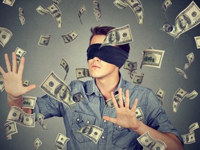 Blindfolded young businessman trying to catch dollar bills banknotes flying in the air isolated on gray wall background. Financial corporate success or crisis challenge concept