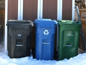 A City of Calgary black bin used to collect garbage, a blue recycling bin and a green bin for food and yard waste.