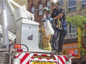 A London firefighter descends from a ladder truck Sunday with what appeared to be a bagged pipe and a bagged knife after police called in the fire department to retrieve evidence of a serious crime from the rooftop of the historic former London and Western Trusts building on Richmond Street near York Street.