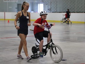 Volunteer Alyssa Malskaitis walks briskly to keep up with nine-year-old Kaden Herrington on an adapted bicycle. Herrington is one of the participants in the iCan Bike program, hosted by the Thames Valley Children's Centre at the Stronach Community Centre this past week. (SHANNON COULTER, The London Free Press)