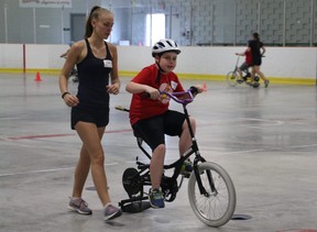 Volunteer Alyssa Malskaitis walks briskly to keep up with nine-year-old Kaden Herrington on an adapted bicycle. Herrington is one of the participants in the iCan Bike program, hosted by the Thames Valley Children's Centre at the Stronach Community Centre this past week. (SHANNON COULTER, The London Free Press)
