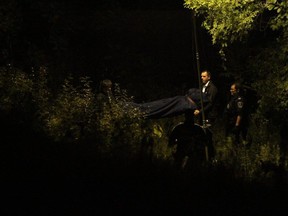 London police investigators assist members of the coroner's office as they remove a body found near the Thames River off of Wortley Road Friday night. DALE CARRUTHERS / THE LONDON FREE PRESS