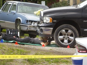 A London police forensic officer takes photos underneath a black pickup truck involved in an incident on Kitchener Avenue in London on Tuesday. (MIKE HENSEN, The London Free Press)