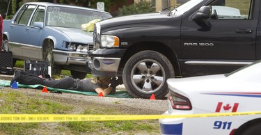 A London police forensic officer takes photos underneath a black pickup truck involved in an incident on Kitchener Avenue in London, Ont.  on Tuesday August 21, 2018. (MIKE HENSEN, The London Free Press)