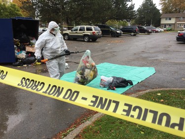 A police investigator combs through garbage in a dumpster at a Marconi Boulevard parking lot where a man was shot Sunday morning. (Dale Carruthers/The London Free Press)