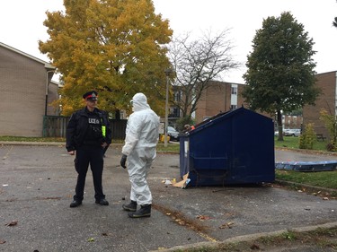 A police investigator combs through garbage in a dumpster at a Marconi Boulevard parking lot where a man was shot Sunday morning. (Dale Carruthers/The London Free Press)