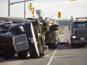 A semi tractor-trailer lays on its side on Veteran's Memorial Parkway after what police say was a slow roll-over caused by a shifted load of  sand and caused no injuries. Tow truck operators were busy removing bags of the sand from the trailer, as the southbound lanes of Veterans Memorial were closed from Wilton Grove to the 401in London, Ont. on Wednesday. Police expected the road to remain closed for 6 hours to remove the load and move the tractor trailer.  Mike Hensen/The London Free Press/Postmedia Network