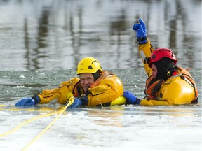 Karl Robb, right, puts a sling around and under the armpits of fellow firefighter Steph Rodowa, who was waiting at the edge of the ice, to be "rescued." The two were part of a contingent of London firefighters training and getting their certification in ice rescue in the frigid waters of the Thames River near the boat launch at Riverside Drive and Wonderland Road on Tuesday. (Mike Hensen/The London Free Press)