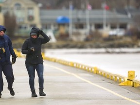 Kevin Boss and Julie TerVrugt of London stagger and hold on to their hoods as they walk into the strong southwest winds along Kettle Creek in Port Stanley early on Sunday.  TerVrugt said they, "come out every Sunday for a stroll...today is a little windier," TerVrugt said they came out earlier in the day to avoid the worst of the forecast winds that were expected Sunday afternoon. Mike Hensen/The London Free Press