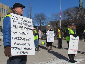 Protesters carrying signs and wearing yellow safety vests gather Saturday morning on the sidewalk in front of Sarnia City Hall in opposition to policies of Canada's federal government.