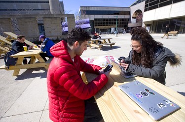 Hadi Kiani and Veronica Botuick enjoy the bright sunshine while using their phones on one of the picnic tables at Western University's concrete beach in London, Ont. The bright sun and mild weather brought Londoners out to embrace the spring-like temperatures. Photograph taken on Tuesday March 19, 2019.  Mike Hensen/The London Free Press/Postmedia Network