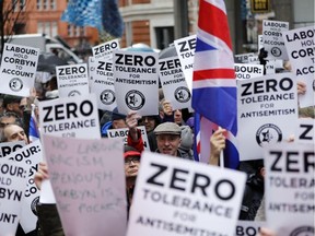 In this file photo taken on April 08, 2018 People hold up placards and Union flags as they gather for a demonstration organised by the Campaign Against Anti-Semitism outside the head office of the British opposition Labour Party in central London on April 8, 2018. - Britain's main opposition Labour party is in turmoil over mounting allegations of anti-Semitism on leftist leader Jeremy Corbyn's watch -- and the party's way of dealing with the issue. The row has exposed deep divisions between Labour members denouncing Corbyn's complacency, and his hard left supporters defending him to the hilt. Nine MPs have quit the party in recent weeks to sit as independents, with many citing alleged anti-Jewish racism seeping through Labour's ranks as a primary reason. One of them, the Jewish lawmaker Luciana Berger, received death threats amid a slew of abuse. (TOLGA AKMEN / AFP/GETTY IMAGES)