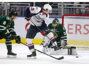 Daniel D'Amico of the Windsor Spitfires tries to deflect a shot past Jordan Kooy of the London Knights while being checked by Riley Coome in the first period of their playoff game at Budweiser Gardens in London on Friday. (Mike Hensen/The London Free Press)