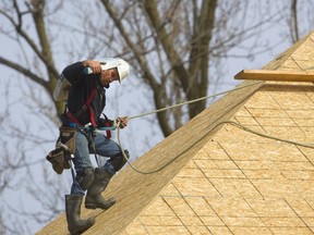 Nick Arnold of Mt. Brydges uses safety ropes and harness while climbing down a roof with a load of shingles while roofing a large home under construction just north of Sunningdale in London, Ont.  Mike Hensen/The London Free Press/Postmedia Network